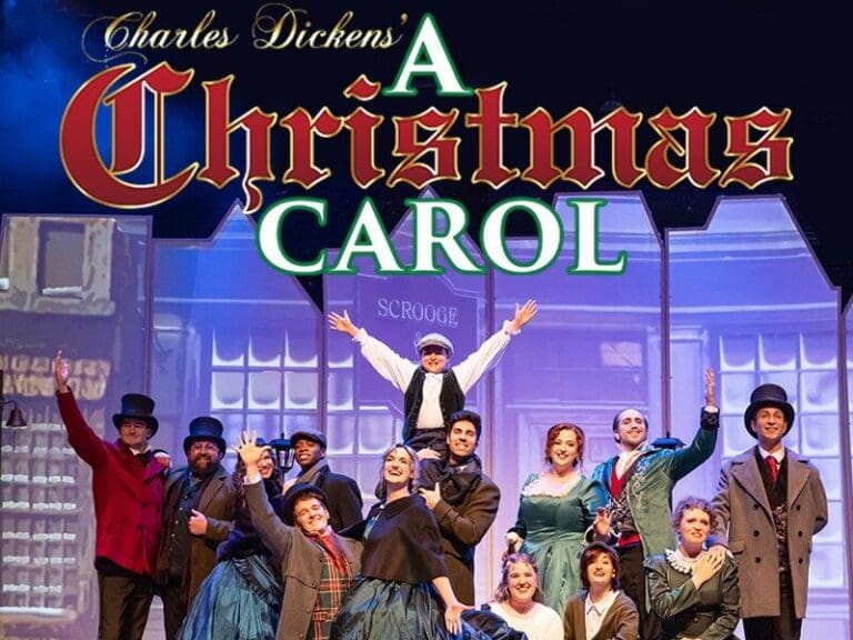 Group of theatre performers in Victorian costumes on stage for A Christmas Carol, with snowy foreground.