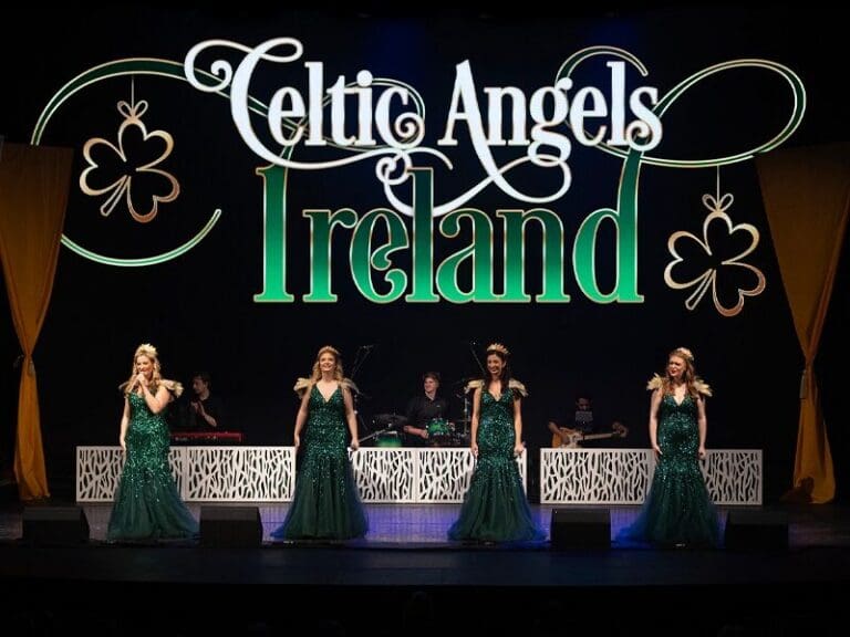 Four female singers in emerald green gowns perform on a stage with a large Celtic Angels Ireland backdrop.