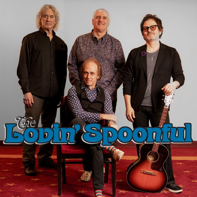 Four-member band photo: one seated front center with a patterned shirt, three standing around him, and a sunburst an acoustic guitar resting beside them. The Lovin' Spoonful logo is at the bottom left.