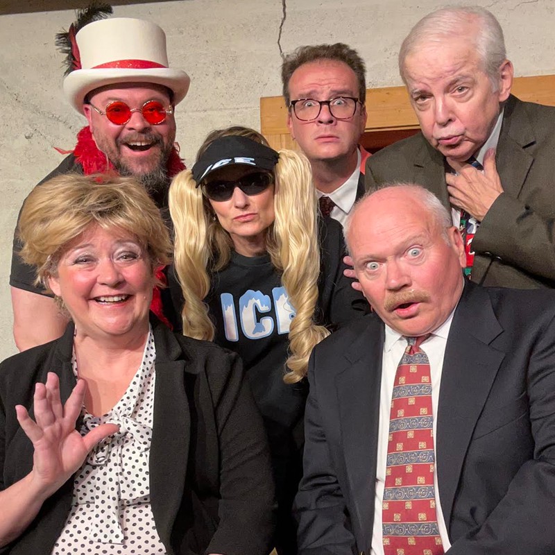 Six adults in quirky costumes posing for a group photo, some wearing wigs, hats, and sunglasses, smiling and making surprised faces.