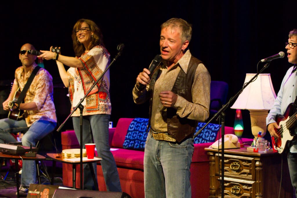 Group of musicians performing on a stage with microphones, guitars, and colorful clothing.