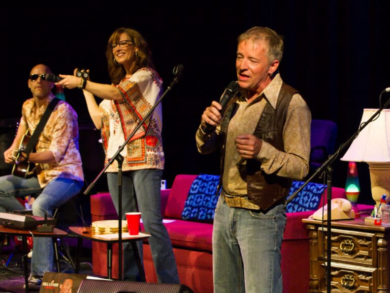 Group of musicians performing on a stage with microphones, guitars, and colorful clothing.